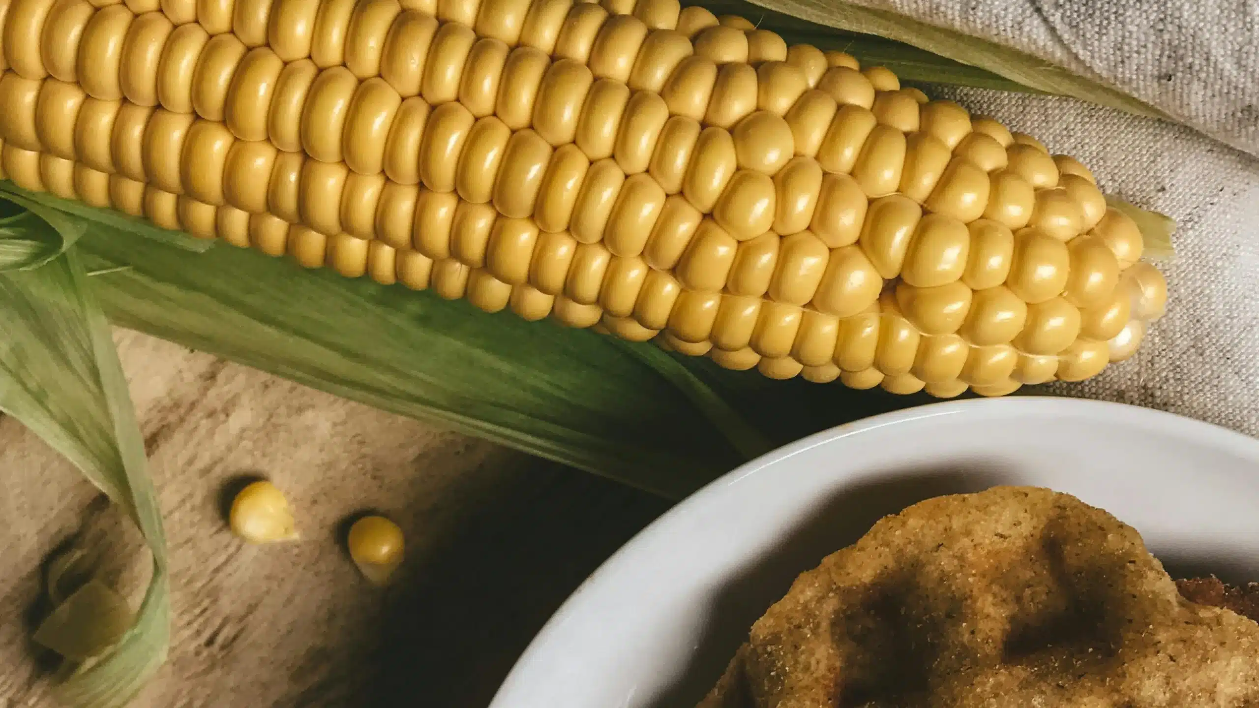 Fresh corn cob with kernels glistening, resting beside golden cornbread slices.