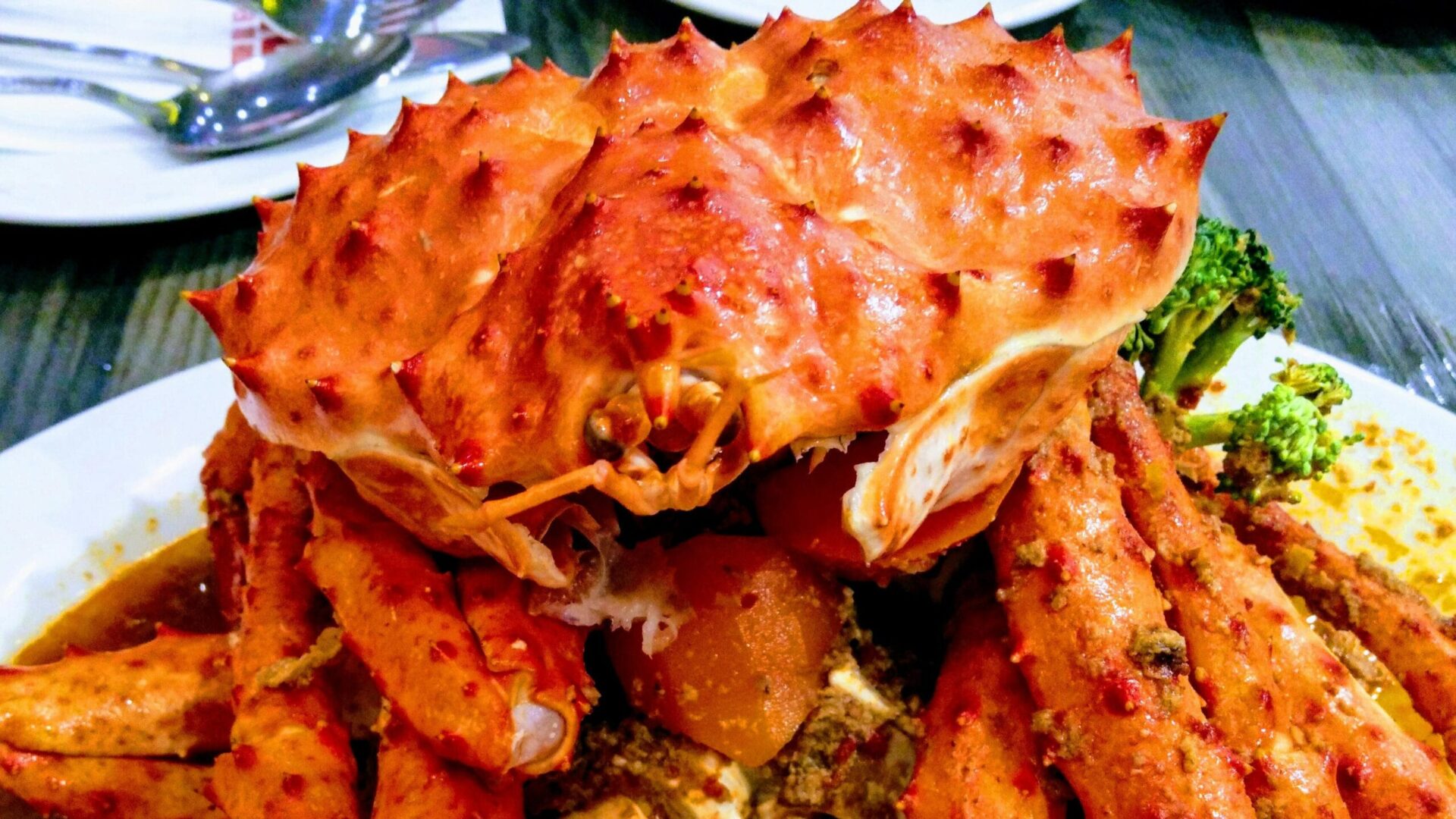 Close-up of a cooked spiny crab from seafood festival served on a plate with a side of broccoli, showcasing its vibrant orange shell and succulent meat.
