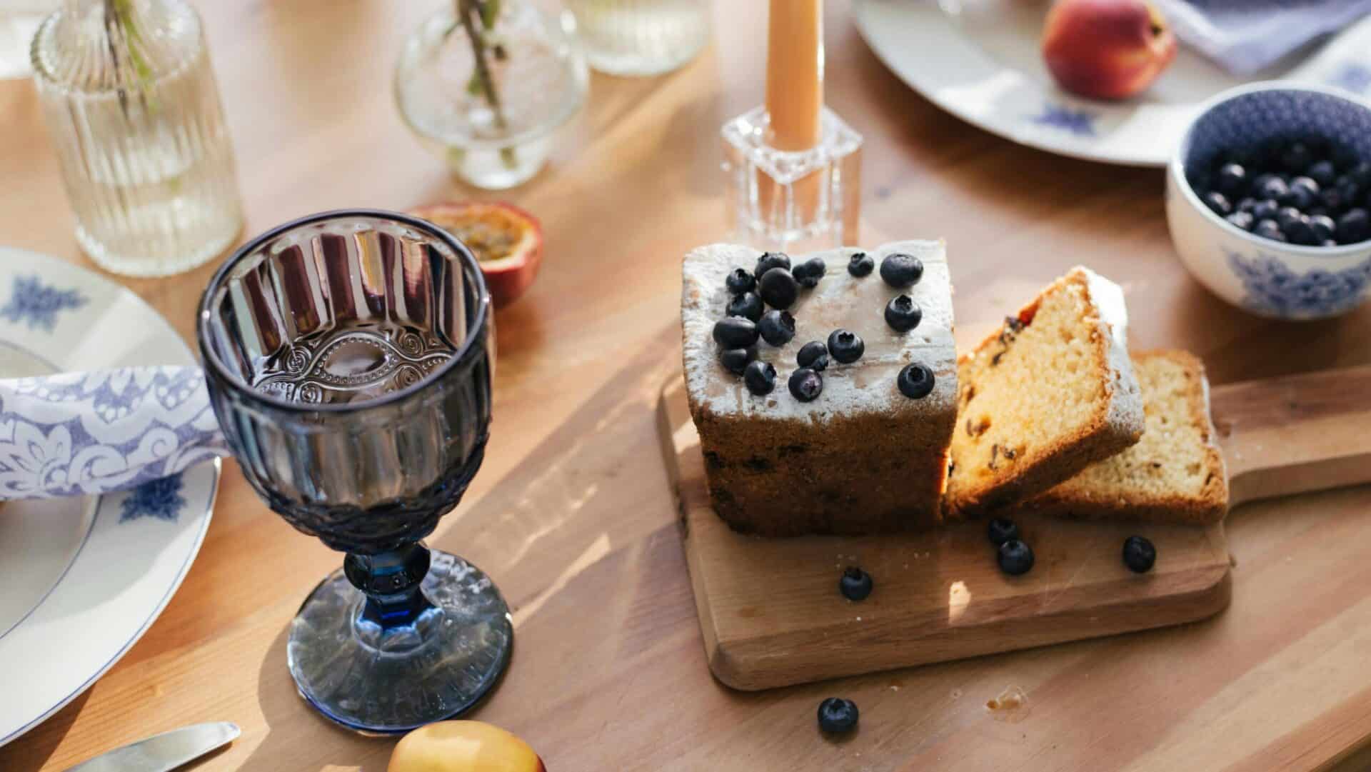 A freshly baked loaf of blueberry lentil bread topped with fresh blueberries, served on a wooden board.