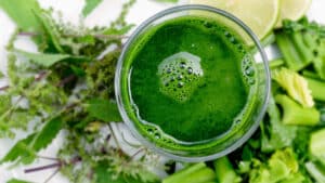 A glass of Detox Island Green Smoothie, featuring a vibrant green blend of spinach, kale, mango, pineapple, and banana, garnished with a fresh mint leaf.