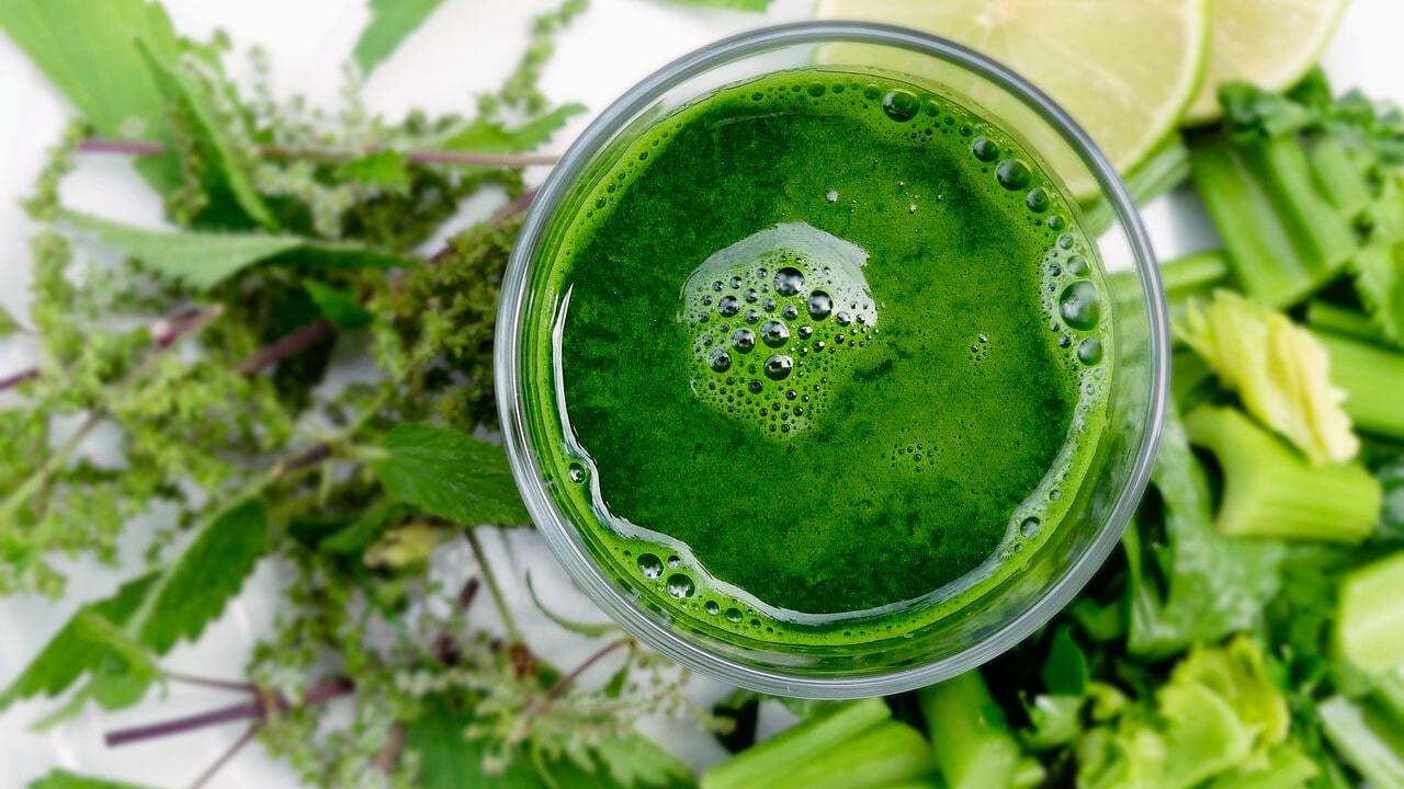 A glass of Detox Island Green Smoothie, featuring a vibrant green blend of spinach, kale, mango, pineapple, and banana, garnished with a fresh mint leaf.