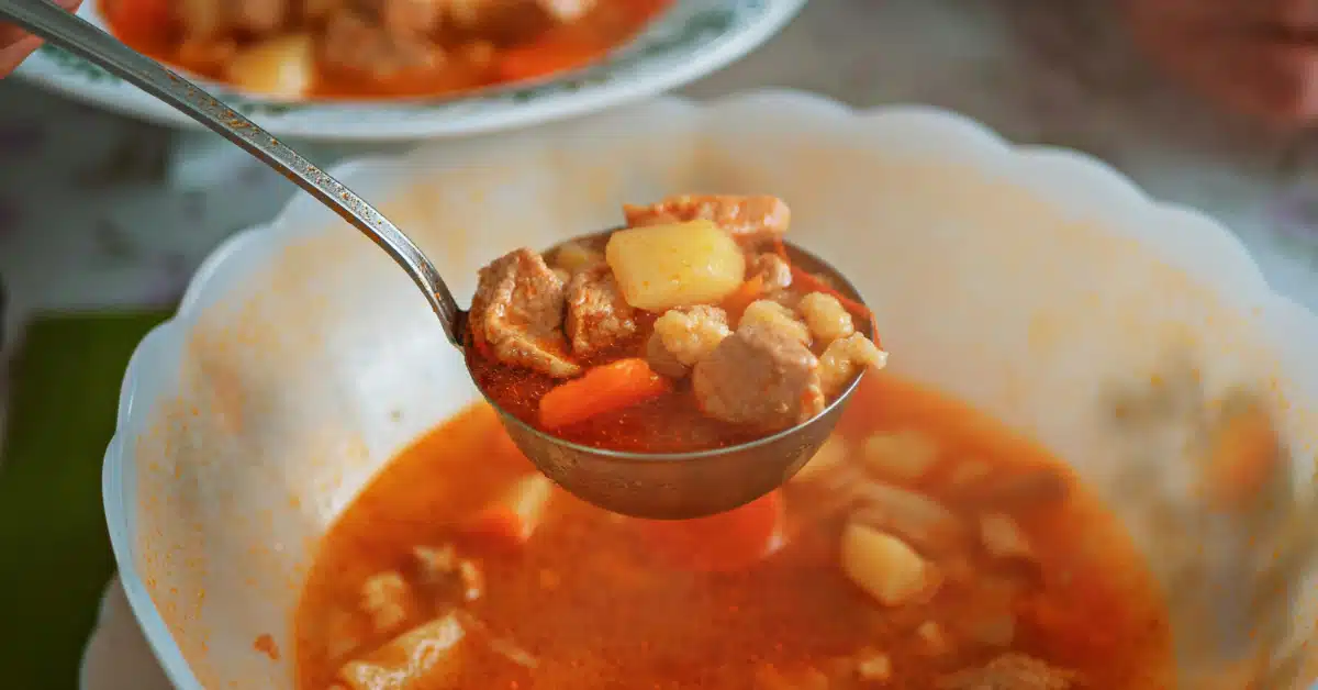 Ladle filled with beef, potatoes, and vegetables from one of the best crockpot soup recipes.